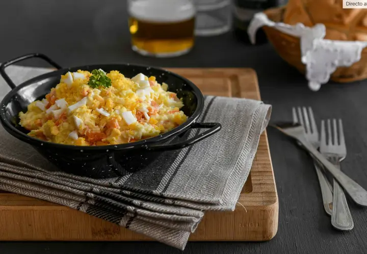 Deliciosa ensaladilla rusa en un cuenco negro, con huevo duro picado y perejil. Acompañada de pan y cerveza.