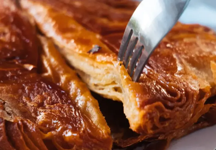 Un tenedor se hunde en un crujiente y caramelizado kouign amann, revelando sus capas hojaldradas.