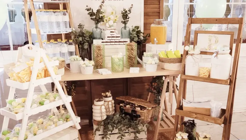 Mesa dulce con dulces, botellas de agua y un dispensador de jugo. Ideas para como hacer un candy bar.