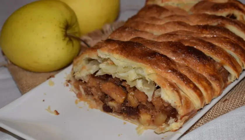 Un delicioso strudel de manzana recién horneado, con su masa dorada y crujiente, relleno de trozos de manzana y pasas.