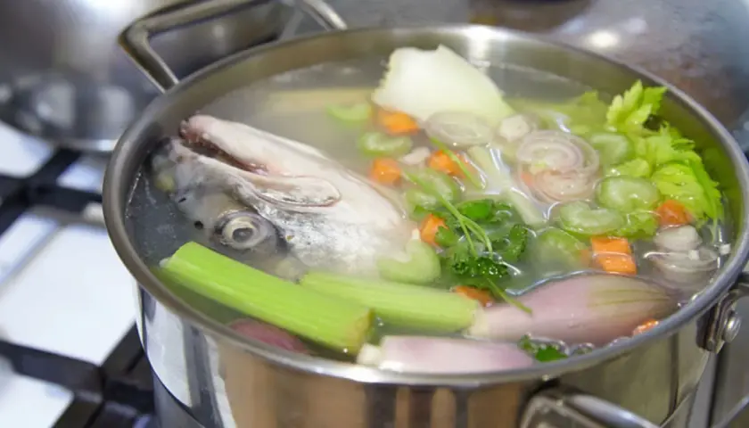 Cabeza de pescado y verduras (zanahoria, apio, cebolla) hirviendo en una olla para hacer un rico caldo de pescado.
