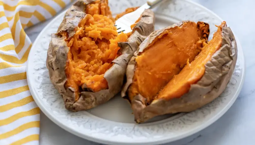 Dos mitades de boniato asado en freidora de aire, servidas en un plato blanco con un tenedor.