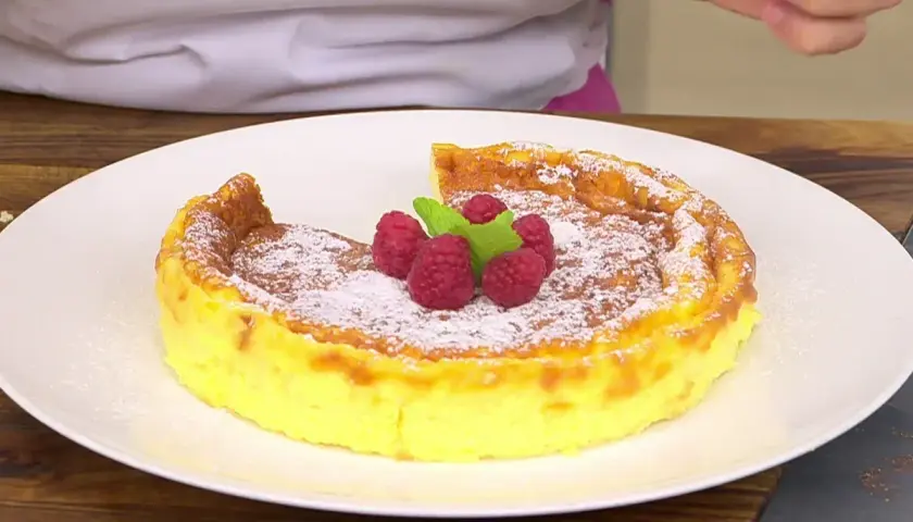 Tarta de queso Eva Arguiñano, dorada y esponjosa, espolvoreada con azúcar glas y decorada con frambuesas y menta.