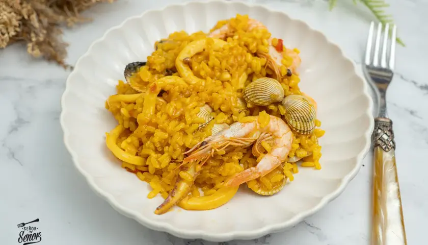 Deliciosa paella de marisco, con gambas, calamares y mejillones, servida en un plato blanco.