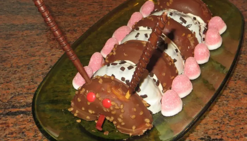 Tarta infantil con forma de oruga hecha de donuts cubiertos de chocolate, decorada con gominolas rosas y barquillos de chocolate.