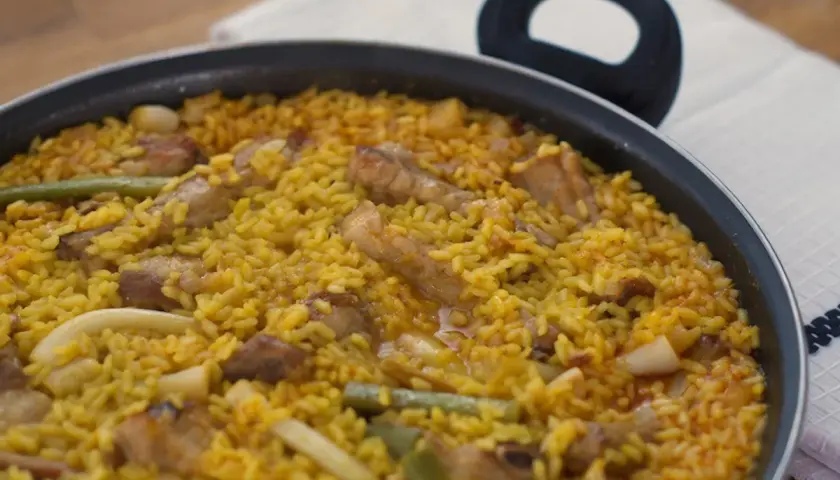 Un delicioso arroz meloso con trozos de carne, judías verdes y calamar en una paellera.