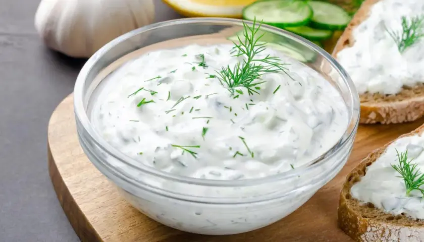 Un tazón de cremosa salsa de yogur con eneldo fresco, perfecto para untar en pan tostado.
