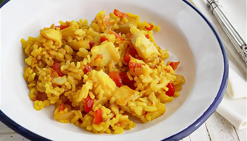 Un plato de arroz con bacalao, pimientos rojos y trozos de pescado blanco. Un delicioso arroz con bacalao listo para disfrutar.