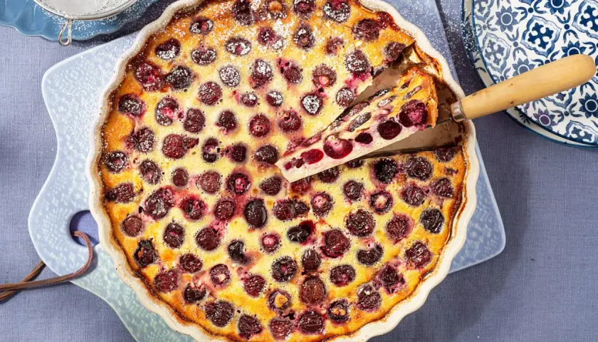Un delicioso clafoutis de cerezas recién horneado, con una porción servida, espolvoreado con azúcar glas.