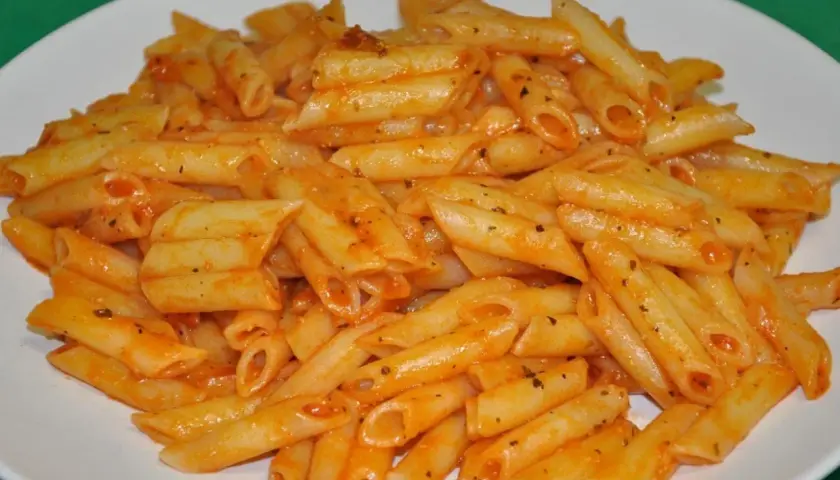 Un plato blanco lleno de macarrones con tomate, cubiertos con una salsa roja y especias.