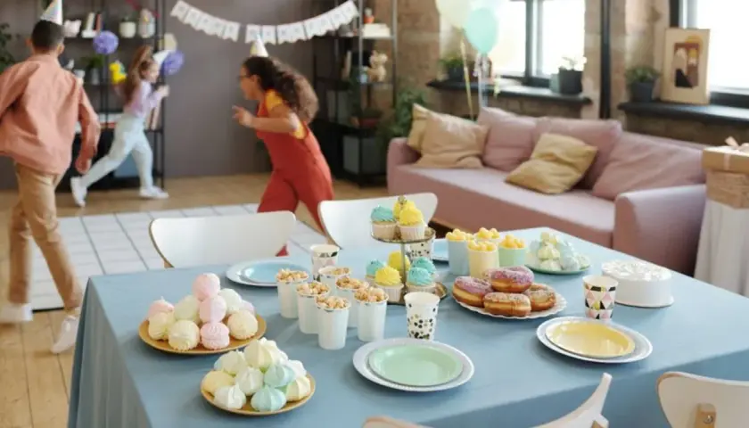 Niños corriendo en fiesta infantil. Mesa con pastel, donas, cupcakes y dulces. ¡Una guía perfecta de como organizar un cumpleaños infantil!