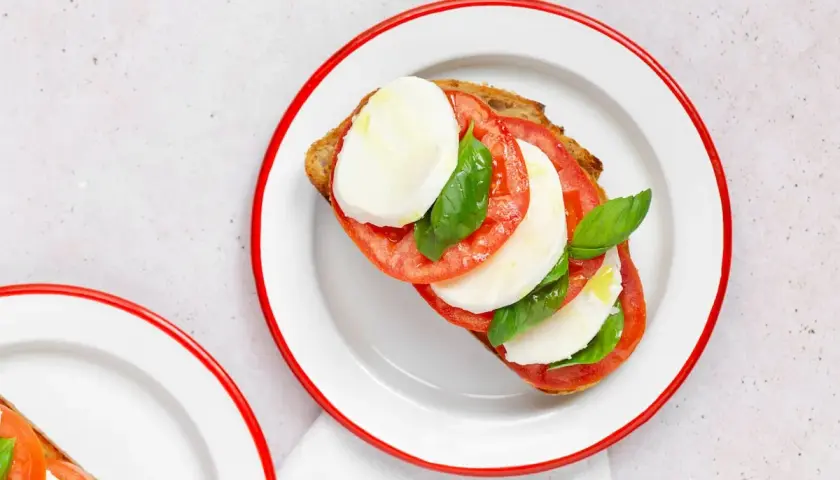 Tostada con rodajas de tomate, mozzarella fresca y albahaca, un clásico de la ensalada caprese.