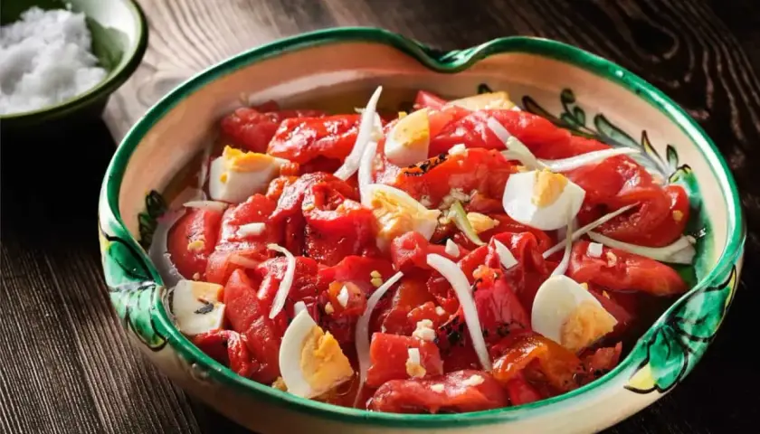 Zorongollo extremeño, una ensalada de pimientos asados, cebolla y huevo duro, servida en una cazuela de barro decorada.