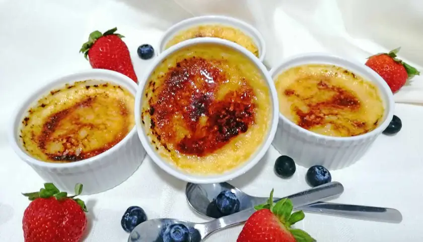 Cuatro cremosos creme brulee con una capa caramelizada, adornados con fresas y arándanos frescos.