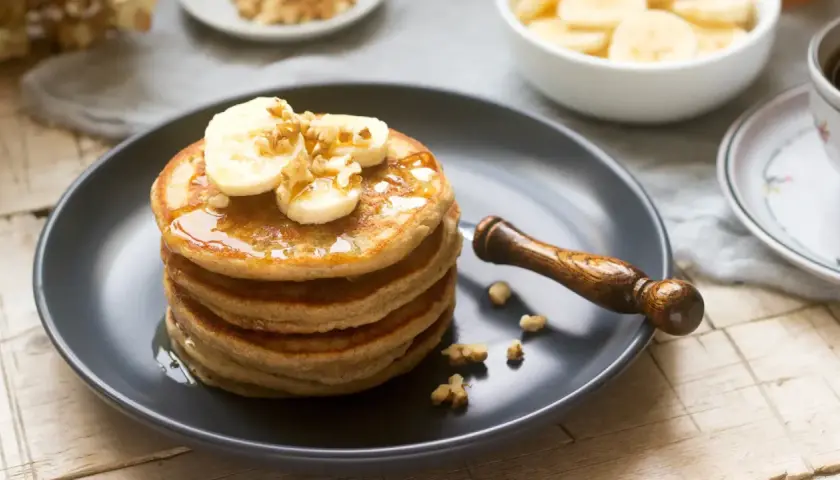 Pila de tortitas esponjosas cubiertas con plátano, nueces y sirope. ¡Una deliciosa receta de tortitas para el desayuno!