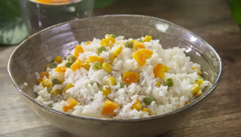 Un tazón de arroz blanco con trozos de zanahoria, guisantes y maíz. Un plato sencillo y colorido de arroz con verduras.