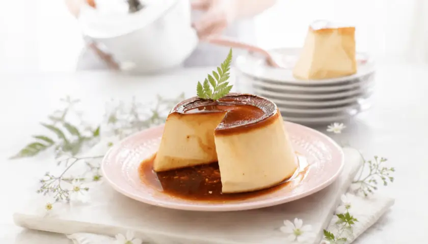 Delicioso flan de queso con caramelo líquido, decorado con una hoja verde y flores delicadas.