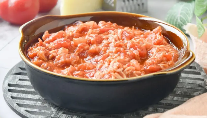 Un tazón de pasta amatriciana, con tomates frescos, queso y rallador al fondo.