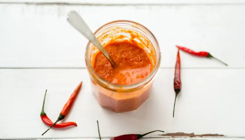 Tarro de cristal con salsa piri piri y chiles rojos alrededor, listo para dar un toque picante a tus platos.