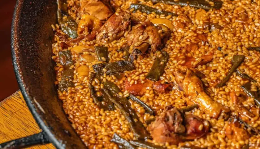 Paella de pollo y judías verdes, con el arroz ligeramente quemado en el fondo, creando un socarrat crujiente.