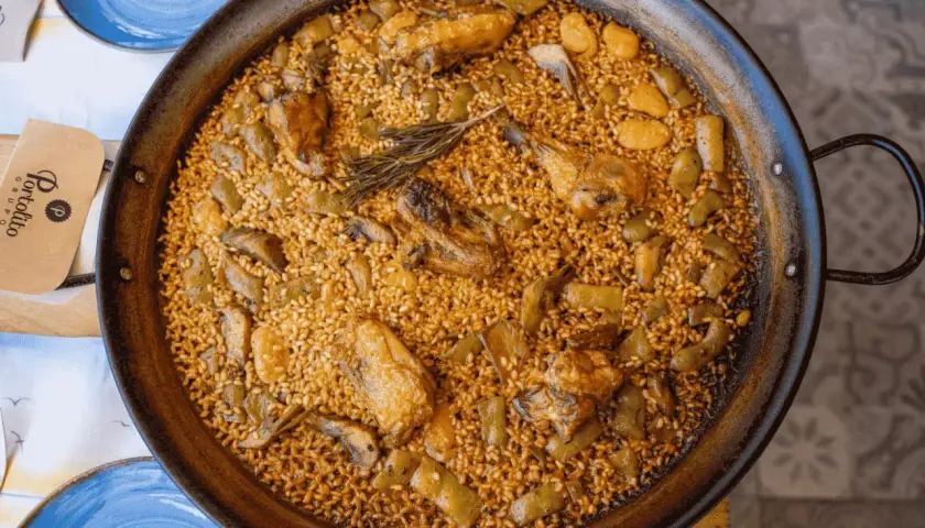 Paella valenciana que lleva pollo, conejo y verduras, con un toque de romero. Un plato tradicional y delicioso.