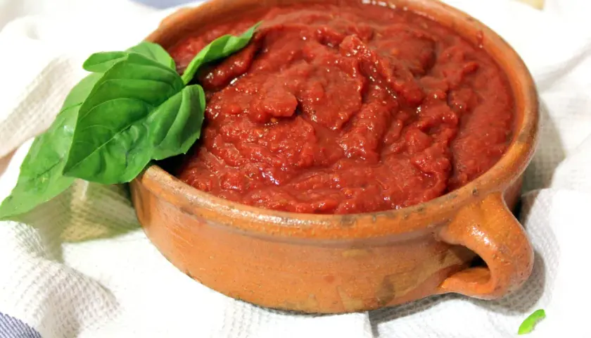 Salsa napolitana casera en cazuela de barro, decorada con hojas de albahaca fresca.
