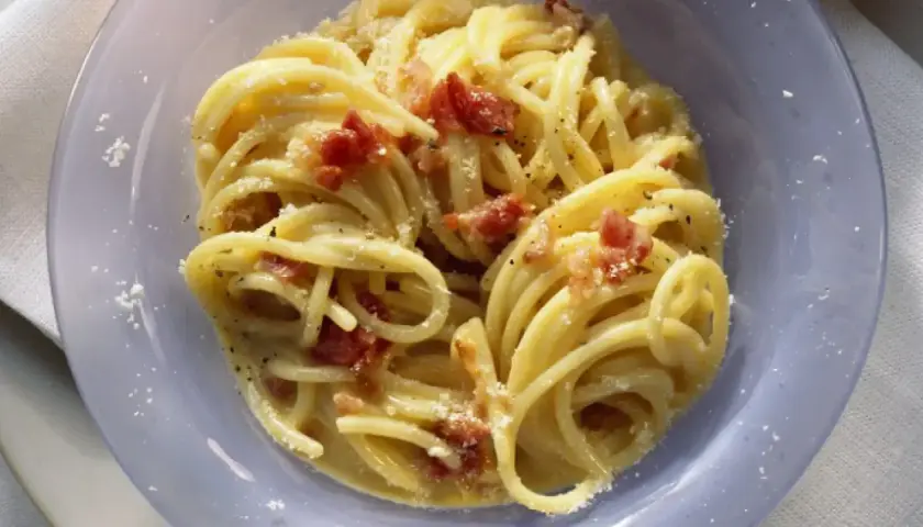 Un plato de pasta carbonara cremoso, con trozos de panceta crujiente y espolvoreado con queso rallado.