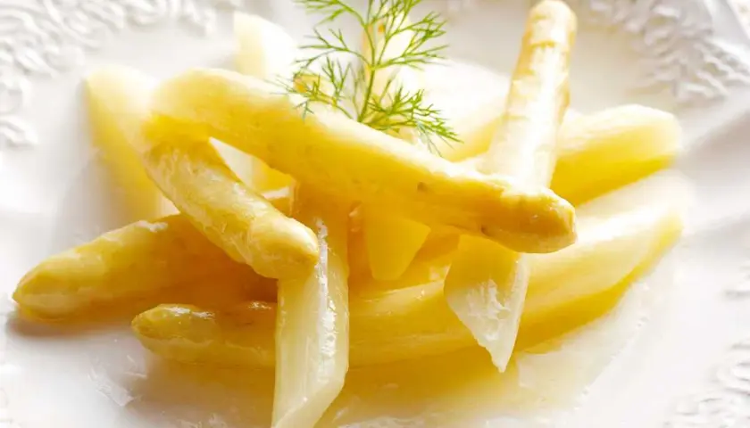Delicados espárragos blancos, tiernos y jugosos, servidos en un plato blanco con un toque de eneldo.