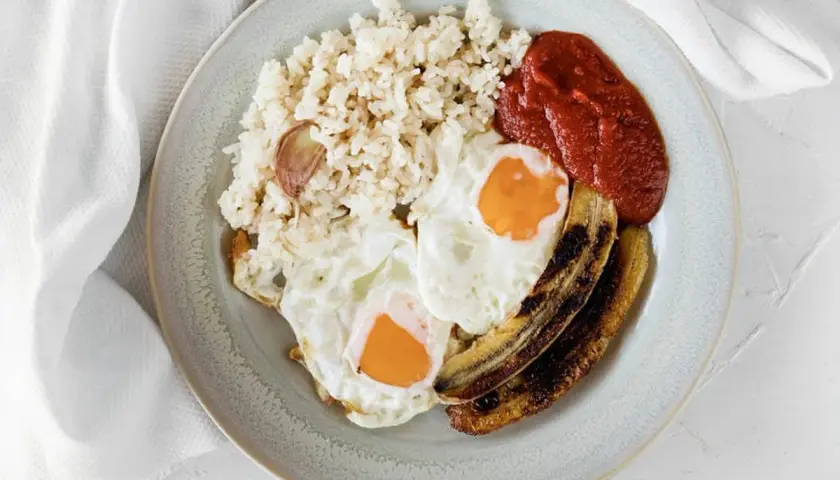 Un plato de arroz a la cubana con dos huevos fritos, plátano maduro frito y salsa de tomate.