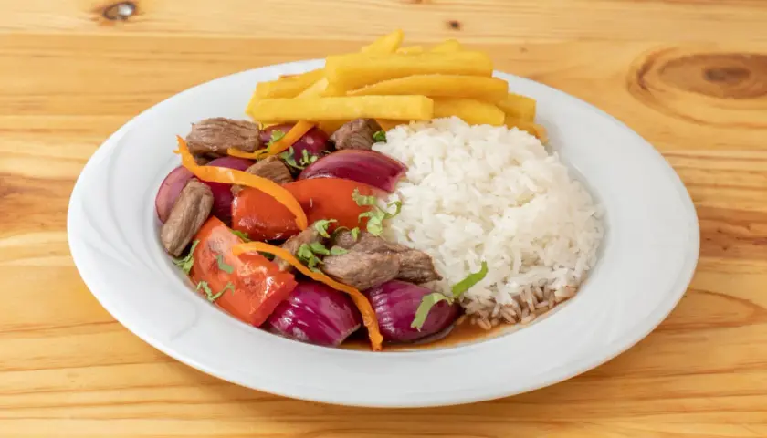 Lomo saltado con arroz blanco, papas fritas, carne, cebolla roja, tomate y cilantro. Un plato peruano delicioso.