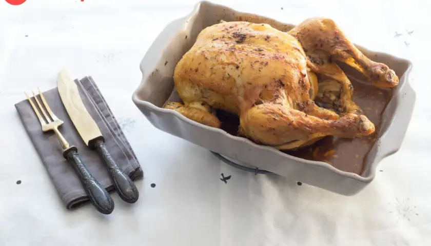 Pollo asado dorado en una fuente, listo para servir. Ideal para tus recetas con pollo. Cubiertos y servilleta a un lado.