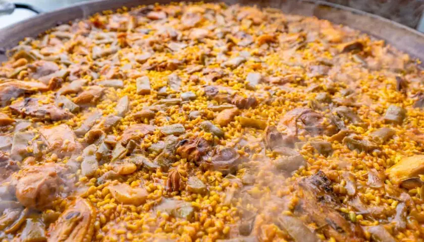 Paella humeante con pollo, judías verdes y trozos de carne. El arroz bomba es el que mejor absorbe el sabor, ideal para esta paella.