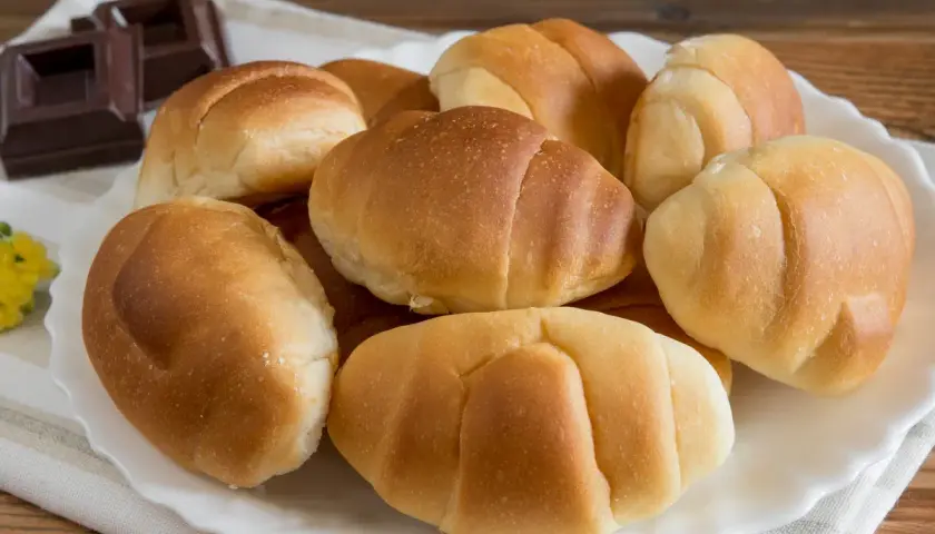 Un plato blanco con pan de leche dorado y suave, junto a trozos de chocolate oscuro.
