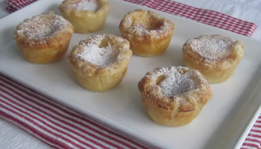 Seis pastelitos de arroz dorados, espolvoreados con azúcar glas, en una bandeja blanca.