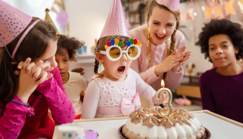 Niños celebran un cumpleaños con pastel y velas. La cumpleañera, con gafas divertidas, sopla la vela. Una temática de cumpleaños para niños llena de alegría.
