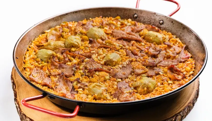 Arroz al horno con trozos de carne y alcachofas, servido en paellera sobre tabla de madera.