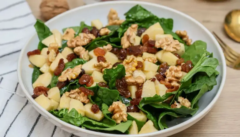 Deliciosa ensalada de espinacas con trozos de manzana, pasas y nueces crujientes.