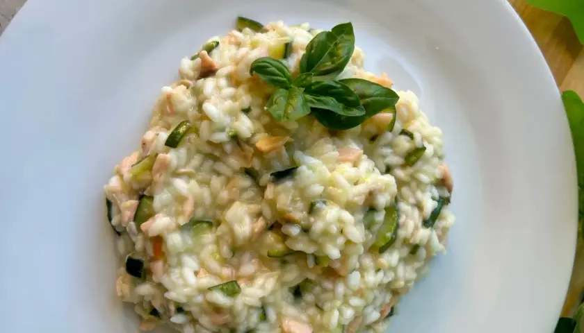 Cremoso arroz a la milanesa con salmón y calabacín, adornado con hojas de albahaca fresca.