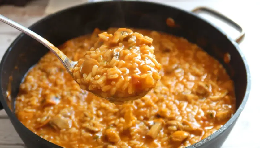 Cuchara sirviendo un delicioso arroz caldoso con pollo y trozos de champiñones.