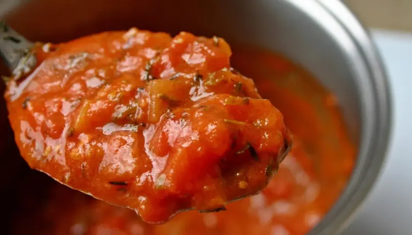 Cuchara llena de sabrosa salsa de tomate casera, con trozos de tomate y hierbas.
