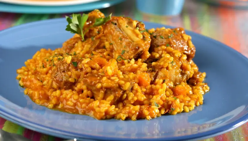 Arroz con costillas, un plato reconfortante con trozos de carne tierna y arroz amarillo, decorado con perejil fresco.