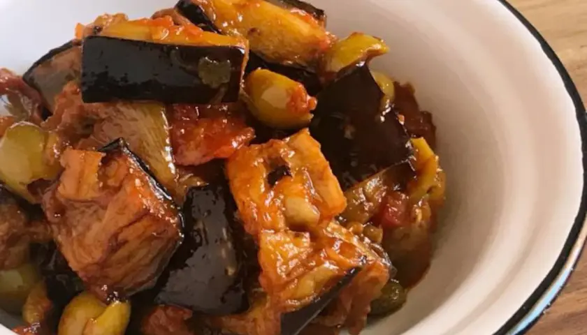 Un plato de caponata siciliana, con berenjenas, aceitunas y tomate, servido en un cuenco blanco.