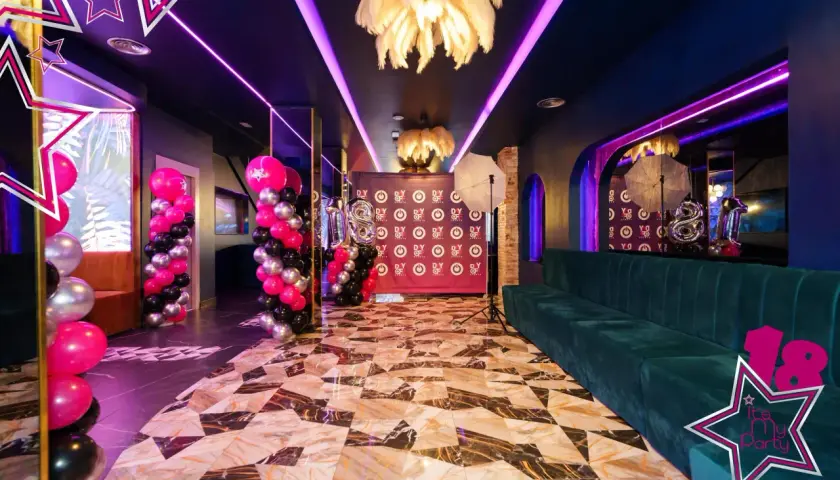 Decoración espectacular con globos rosas, negros y plateados, luces neón y un sofá verde. ¡Ideas para fiesta de 18 años mujer!