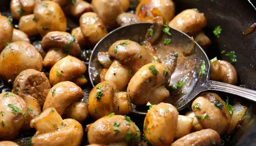 Champiñones salteados con perejil, perfectos para tus recetas con champiñones. Una cuchara sirve para cogerlos.