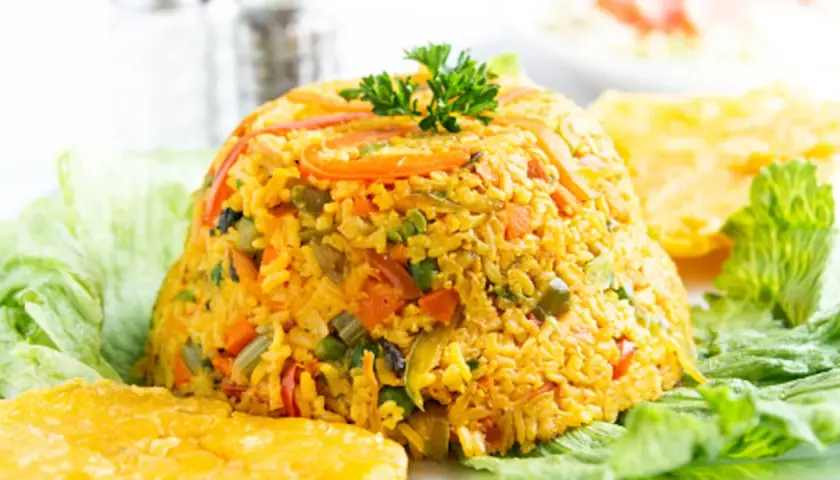 Un montículo de arroz con pollo, adornado con perejil, servido sobre hojas de lechuga y acompañado de plátanos fritos.