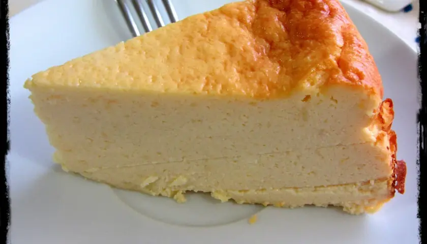 Una rebanada de tarta de queso Philadelphia, con su superficie dorada y cremosa textura, lista para ser disfrutada.