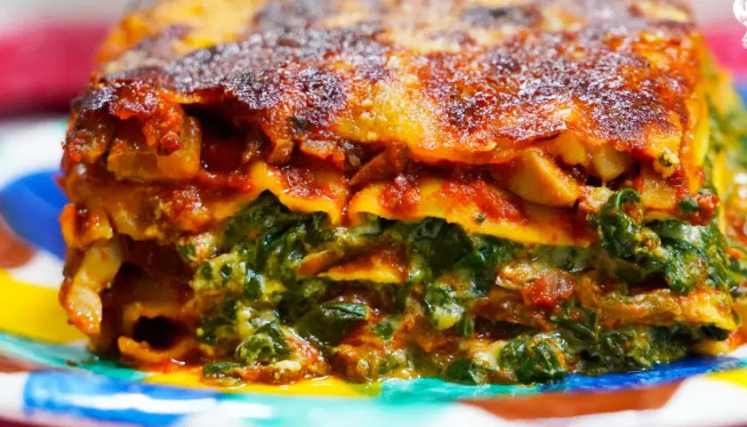 Porción de lasaña de verduras, con capas de pasta, espinacas y salsa de tomate, servida en un plato colorido.