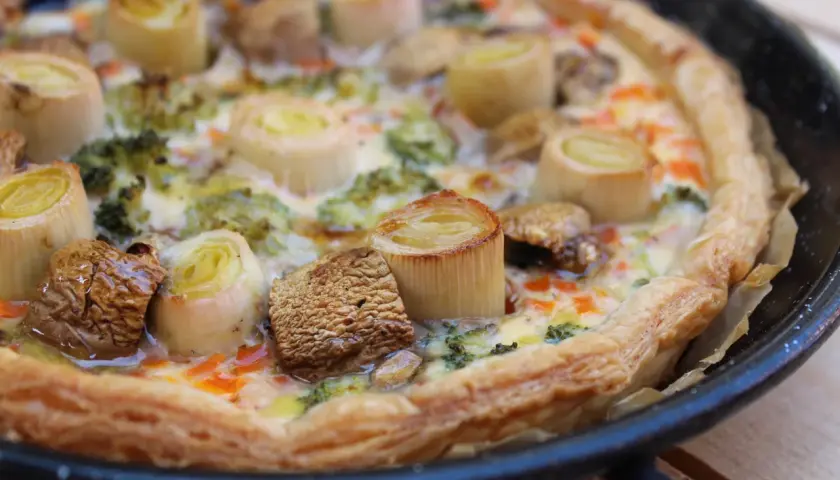 Quiche de verduras recién horneada, con puerros, brócoli y champiñones, lista para disfrutar.