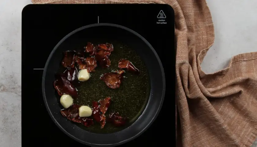 Sartén con aceite, ajos y trozos de pimiento rojo, preparando la base para una salmorreta receta.