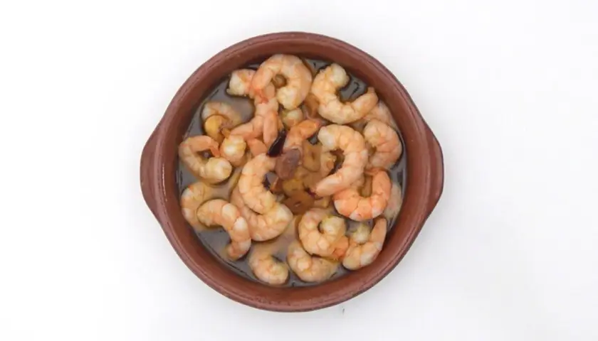 Gambas al pil pil burbujeantes en cazuela de barro, con ajo y aceite de oliva.